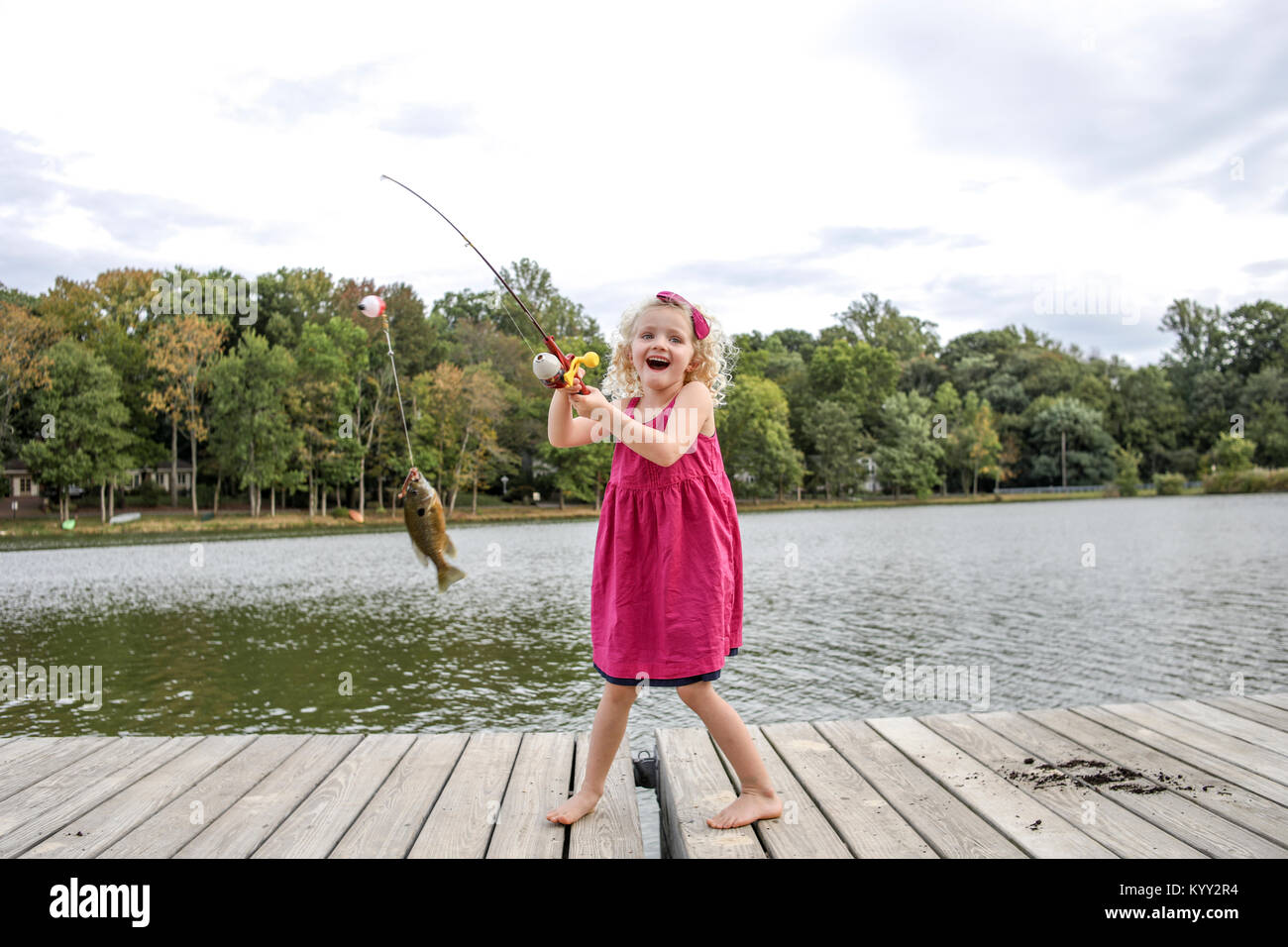 Chica alegre celebración pescado en caña de pescar estando de pie en el  embarcadero de madera en el parque Fotografía de stock - Alamy