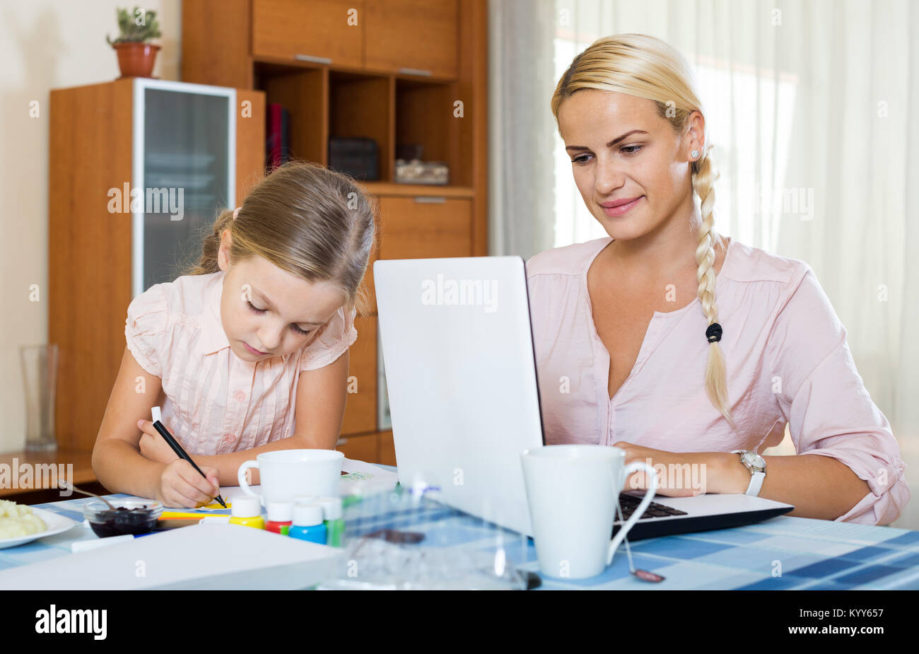 La empresaria americana sonriente navegando por internet en casa, hija dibujo a lápiz Foto de stock