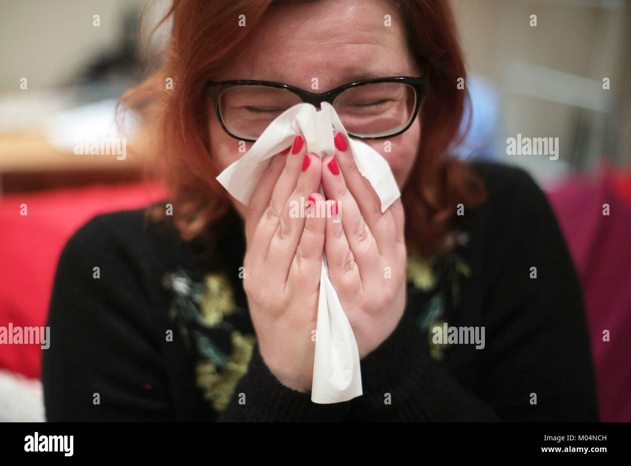 Una mujer con un frío de sonarse la nariz con un pañuelo de papel, en Londres. Foto de stock