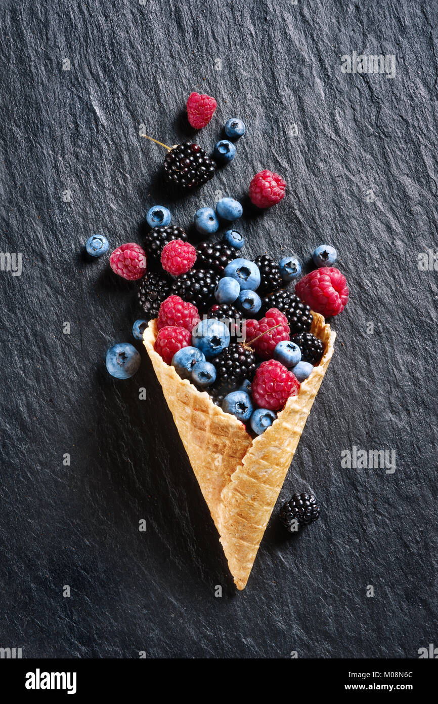 Explosión de diferentes bayas. Foto de Blueberry, blackberry, frambuesa en waffle cono en pizarra negra. Vista desde arriba. Producto de alta resolución. Foto de stock