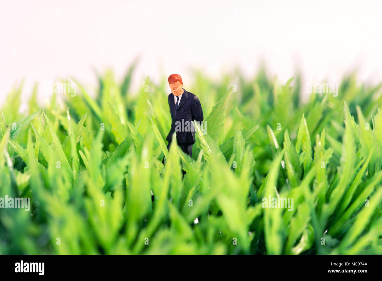 Miniatura de la figura de un hombre de negocios de pie en el pasto verde pensando en busca de inspiración e ideas Foto de stock
