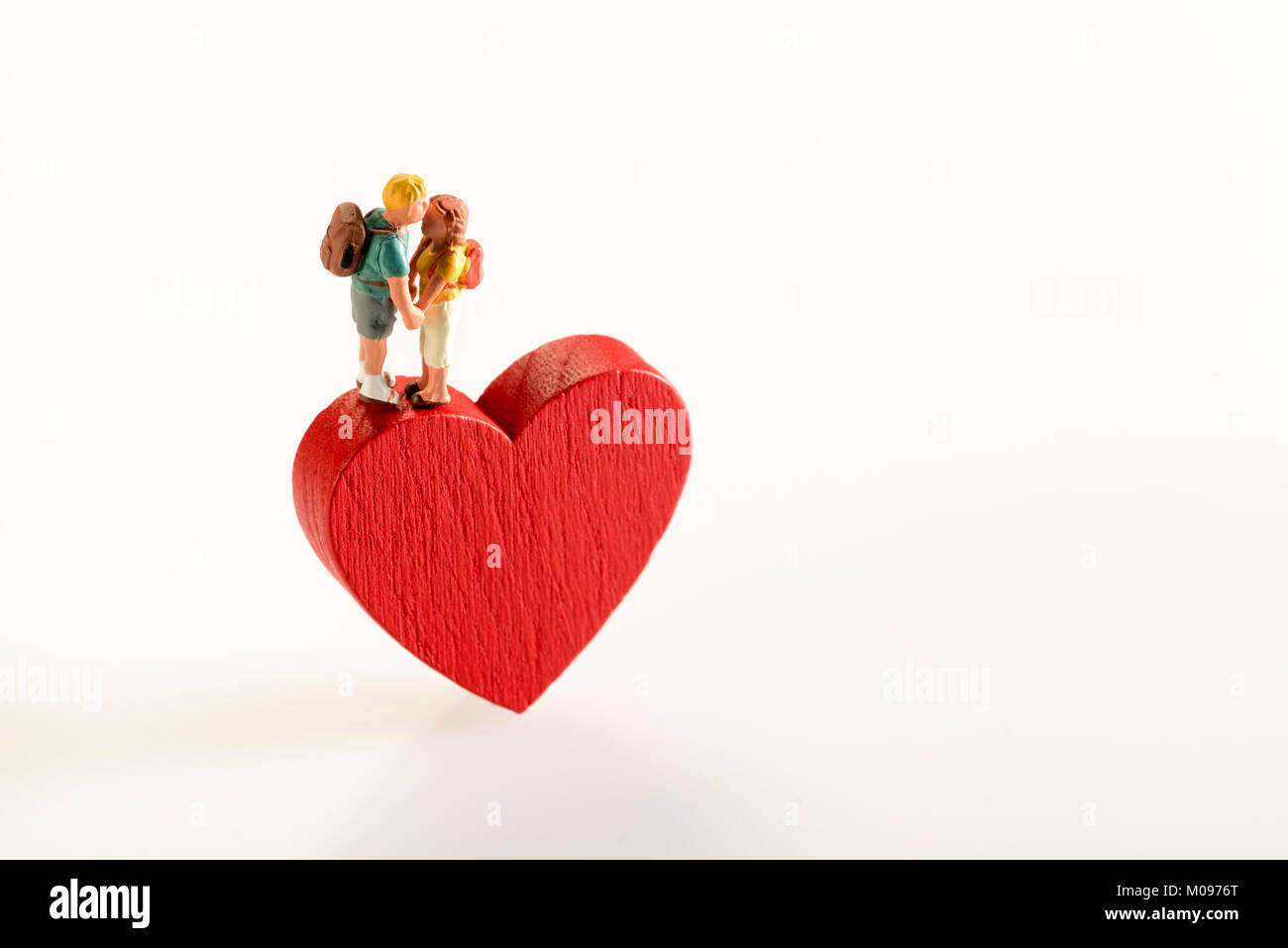 Cierre conceptual de una miniatura de la figura de pareja en el amor cogidos de la mano mientras está de pie sobre un corazón rojo forma de madera contra un fondo blanco para copiar sp Foto de stock