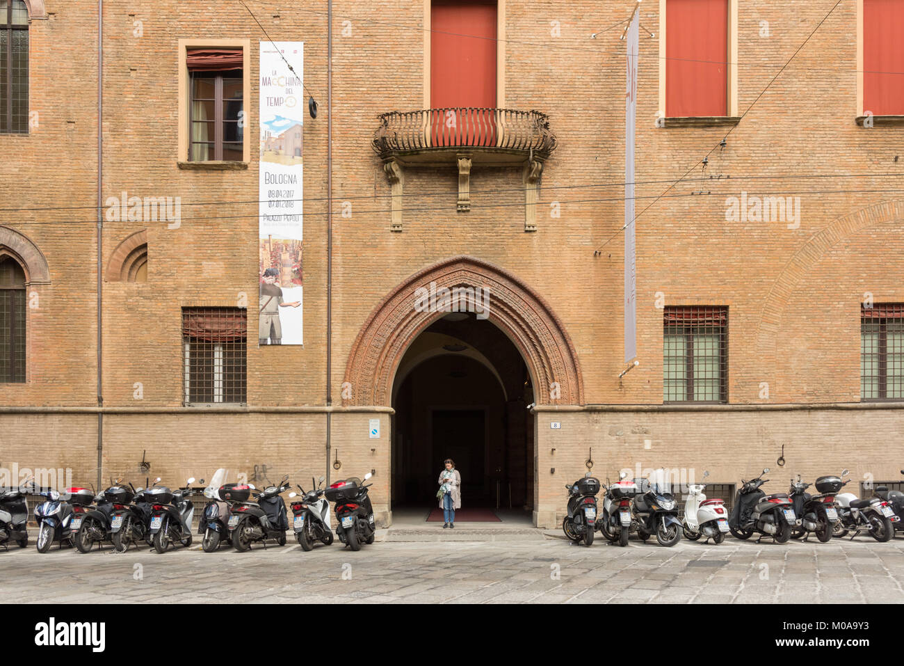 La entrada al museo Palazzo Pepoli en Bologna, Italia con una mujer de pie en la entrada y un montón de scooters y motocicletas estacionados en una fila Foto de stock