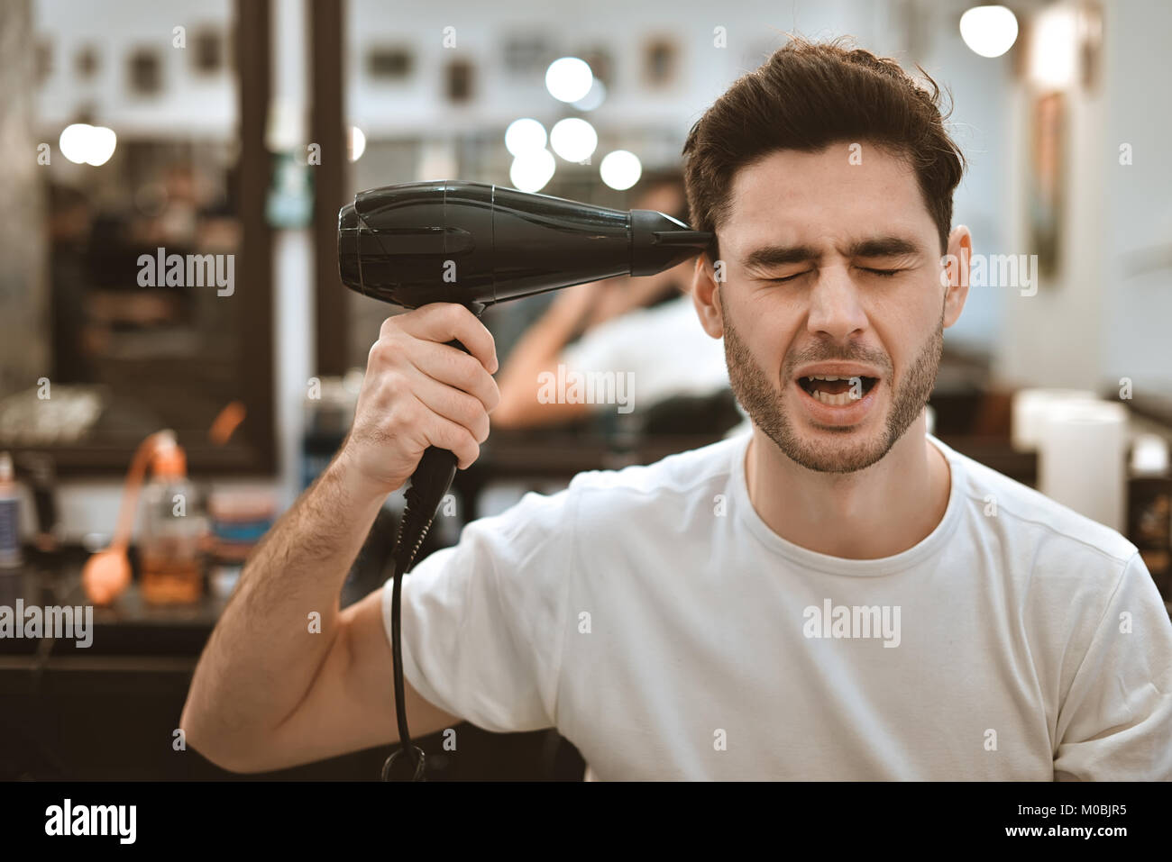 Loco joven hombre elegante con secador de pelo y graciosas expresiones en  la barbería Fotografía de stock - Alamy