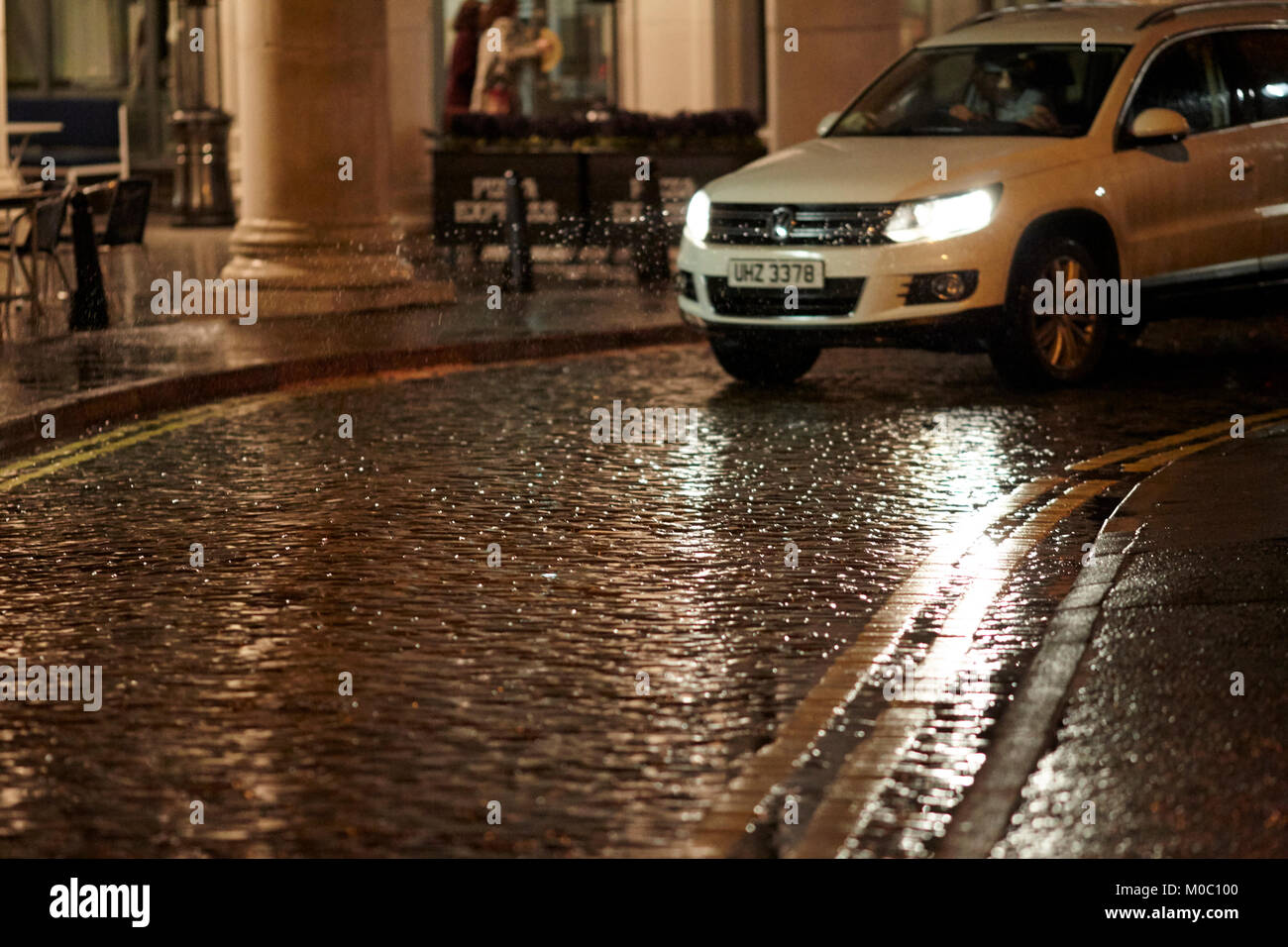 Coche de conducción a lo largo de calles empedradas húmedo por la noche, Belfast, Irlanda del Norte, reino unido Foto de stock