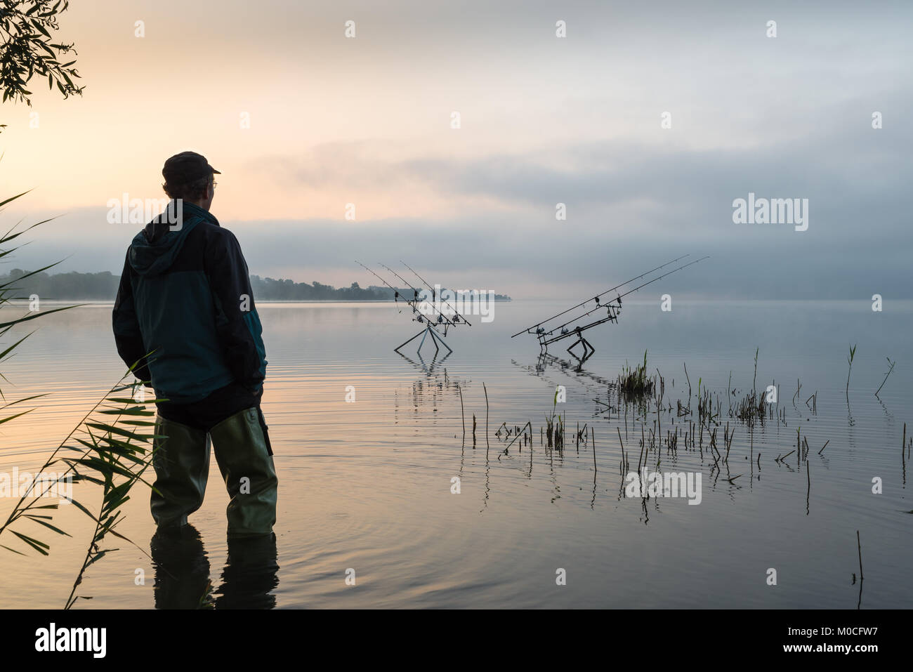 Aventuras de pesca, la pesca de la carpa. Temprano en la mañana con niebla y pescador con botas de caucho Foto de stock