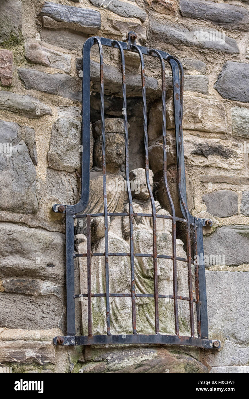 Antigua estatua de piedra medieval en muro de la Virgen con el niño intemperie lejos detrás de las rejas Foto de stock