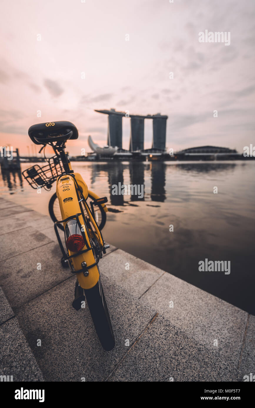OFO moto estacionada enfrente de un cuerpo de agua durante el amanecer en Singapur. Foto de stock