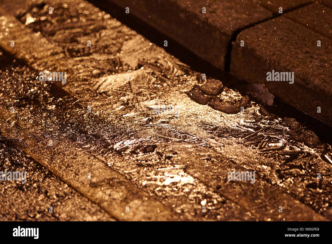 Formación de hielo sobre el agua de alcantarilla en la carretera con el doble de líneas amarillas en la noche en el reino unido Foto de stock