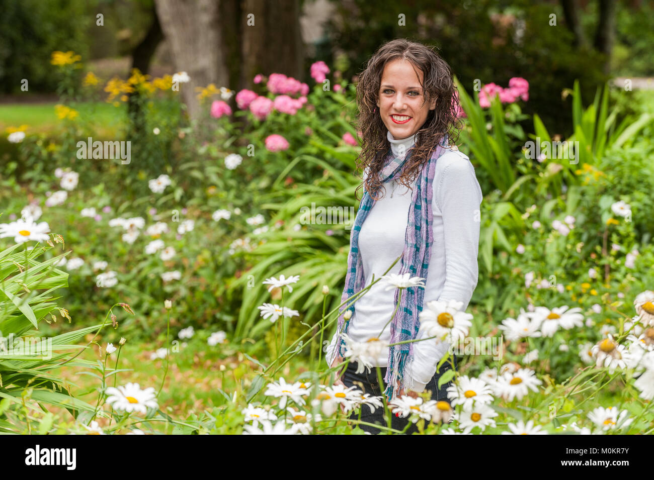 Hermosa modelo sonriente de pie entre las flores en un parque en Cork, Irlanda. Foto de stock