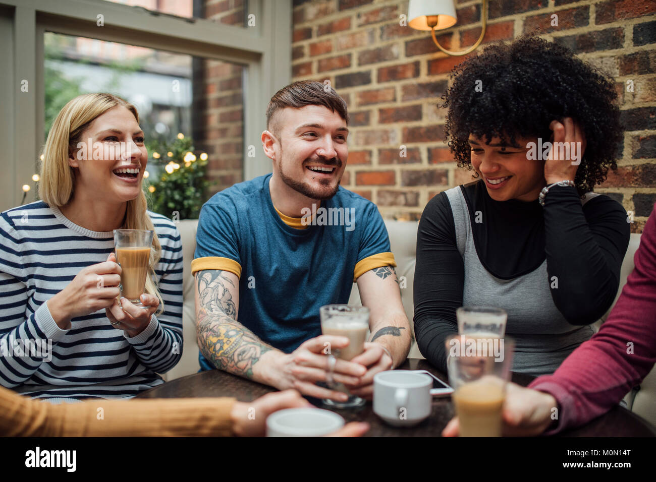 Los amigos son socializar con el café en una cafetería. Se están riendo y  hablando con sus bebidas en sus manos Fotografía de stock - Alamy