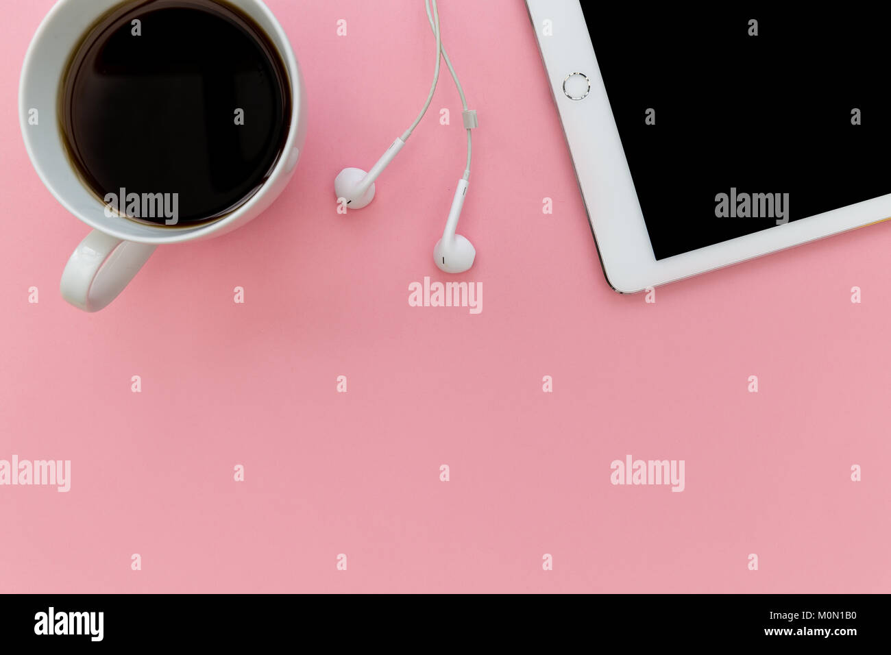 Equipo tablet blanco Auriculares y sobrecarga de la taza de café sobre fondo de color rosa pastel Foto de stock