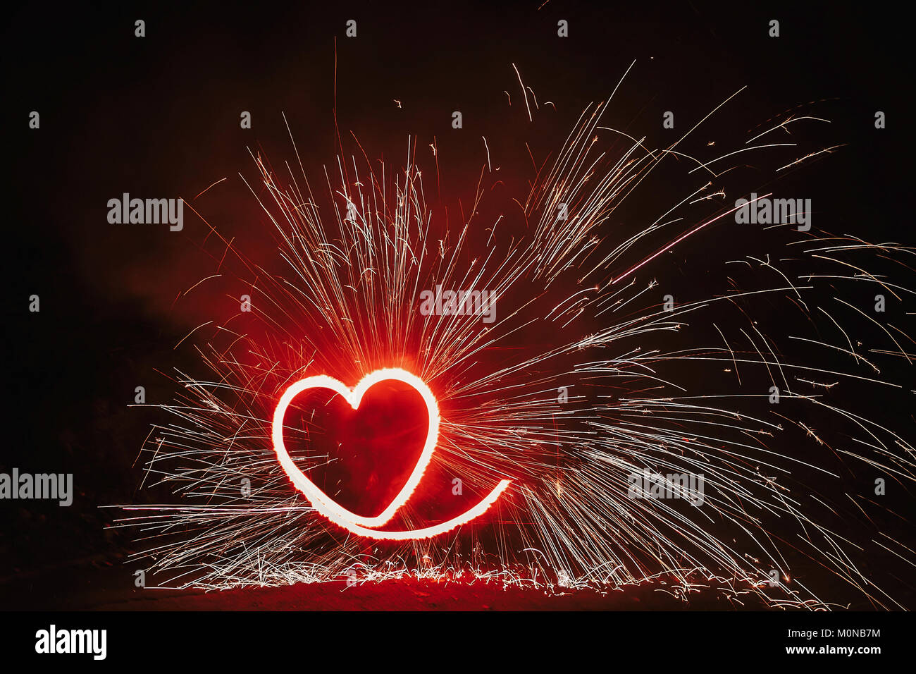 Fuegos artificiales en forma de corazón rojo sobre fondo negro con brillos en la noche. Feliz Día de San Valentín tarjeta corazón ardiente fuego de Bengala. Espacio para texto o boda. Foto de stock