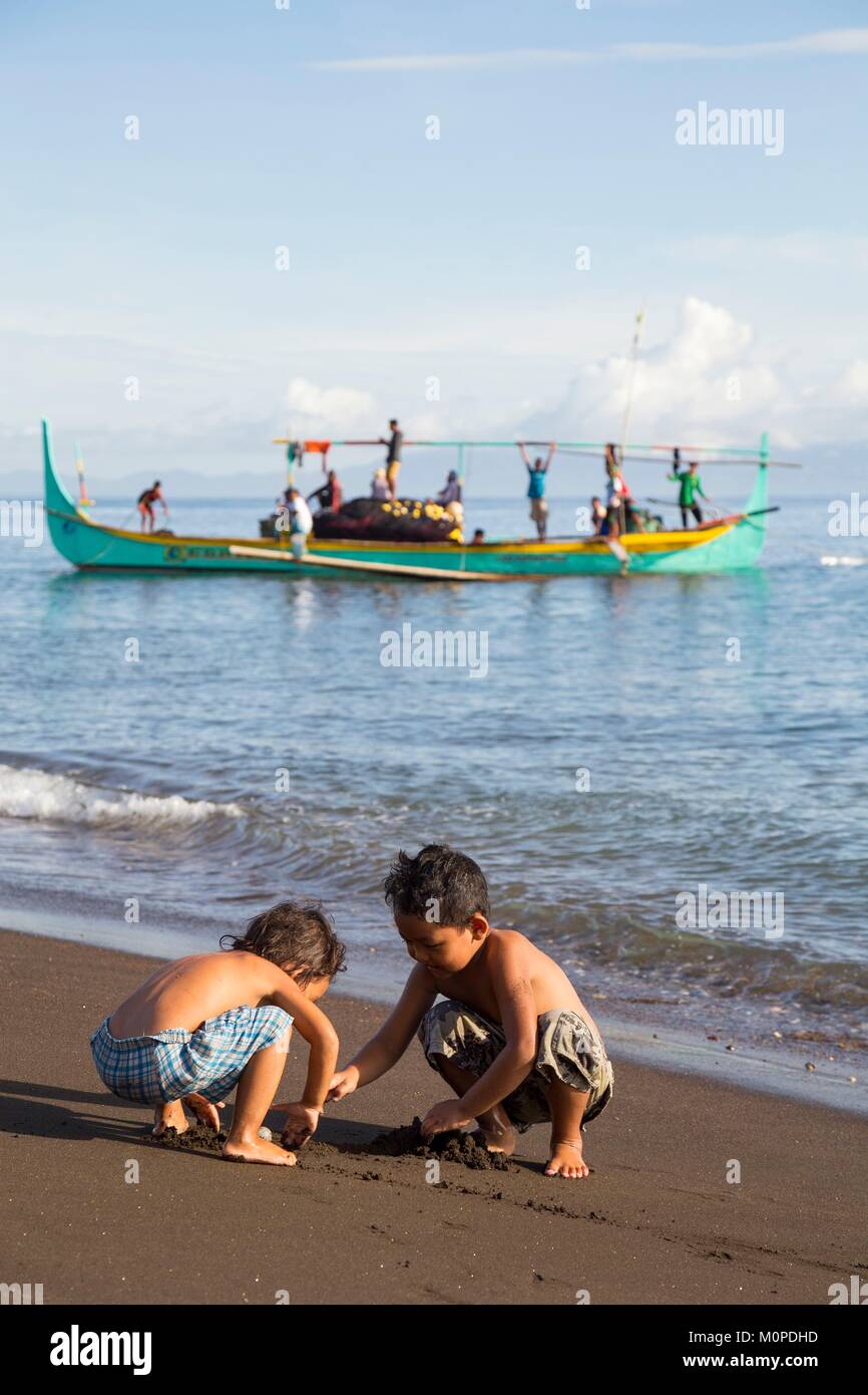 Filipinas, Luzón, Provincia de Albay,Tiwi,Sogod beach,niños jugando en la arena con un barco pesquero ringnet viniendo en segundo plano. Foto de stock