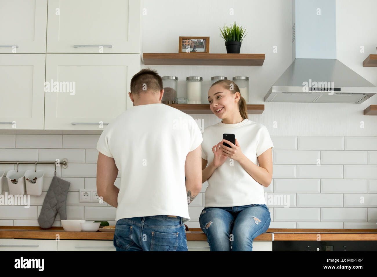 Par disfrutar de cocina, mujer sosteniendo el smartphone mientras el hombre prep. Foto de stock