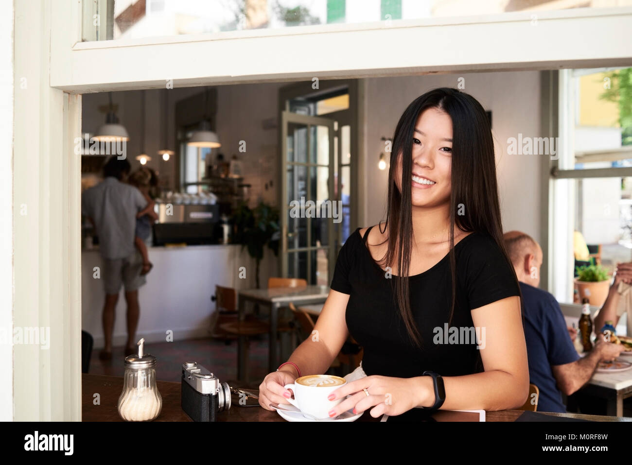 Feliz morena milenario asiático en una cafetería junto a la ventana. Foto de stock