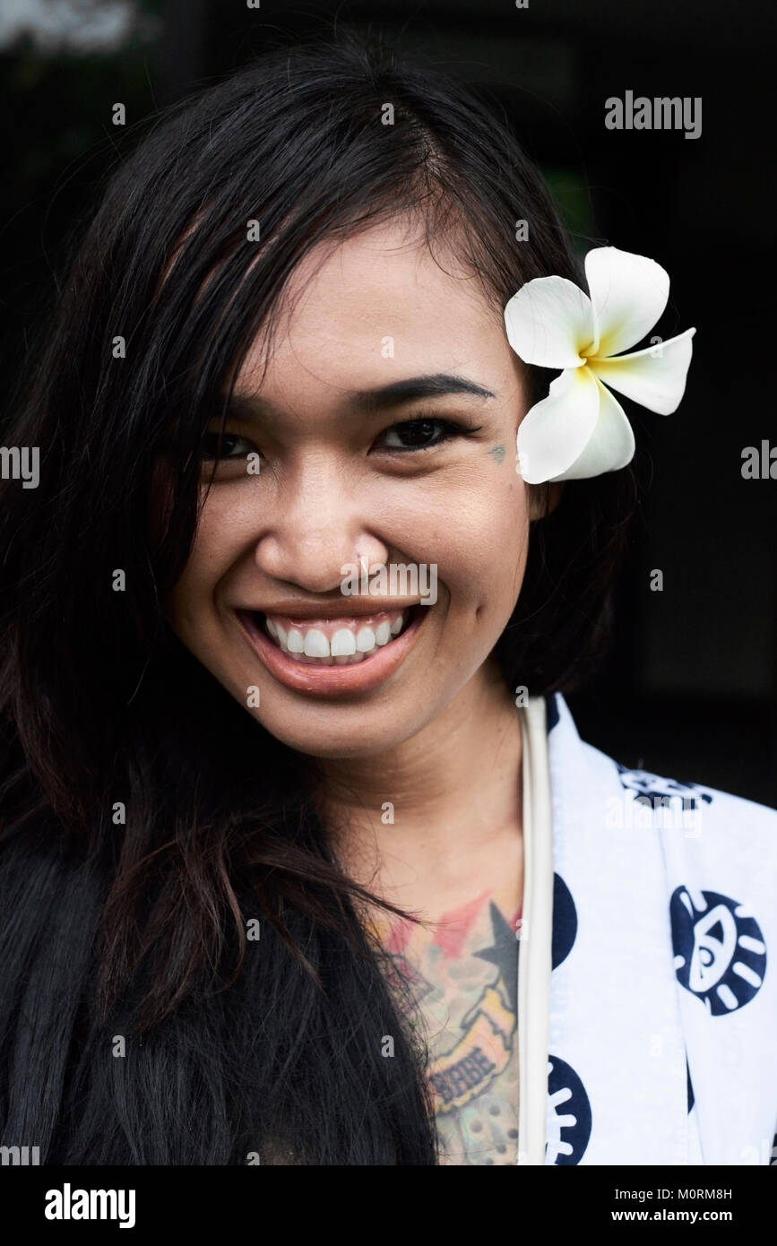 Retrato de una hermosa muchacha morena asiática con flor de smiley en cámara en atuendo de verano. Foto de stock