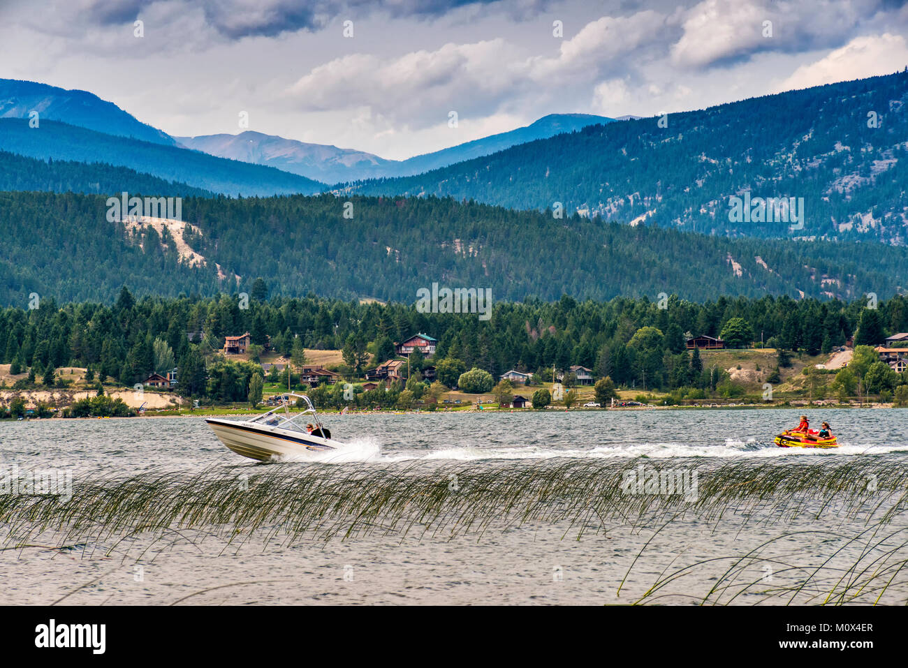 Lancha tirando de la mujer y la niña en el bote de goma, el lago Windermere, Columbia Valley, Purcell Mountains, cerca de Invermere, British Columbia, Canadá Foto de stock