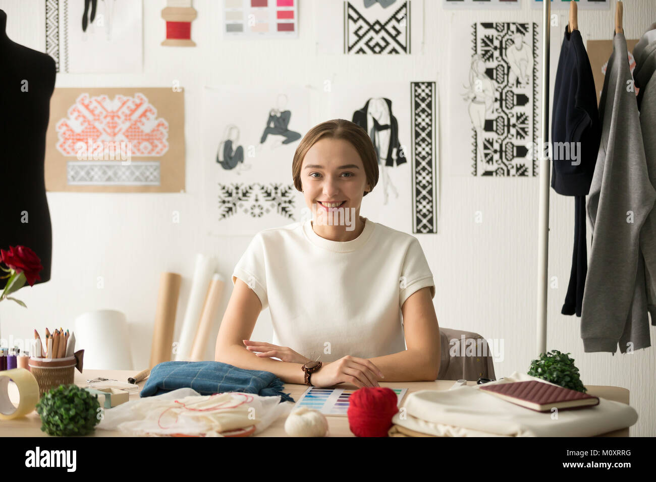 Diseñador de moda atractiva sonriente sentado en el lugar de trabajo buscando Foto de stock