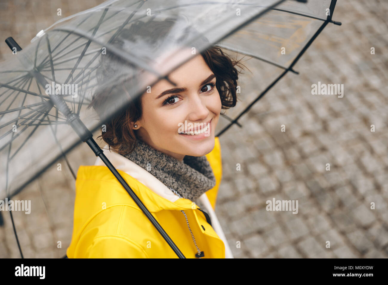 Chica joven con chubasquero amarillo con paraguas transparente en la  ciudad. Joven hermosa mujer con traje de lluvia y gafas mientras camina en  la calle. Con Fotografía de stock - Alamy
