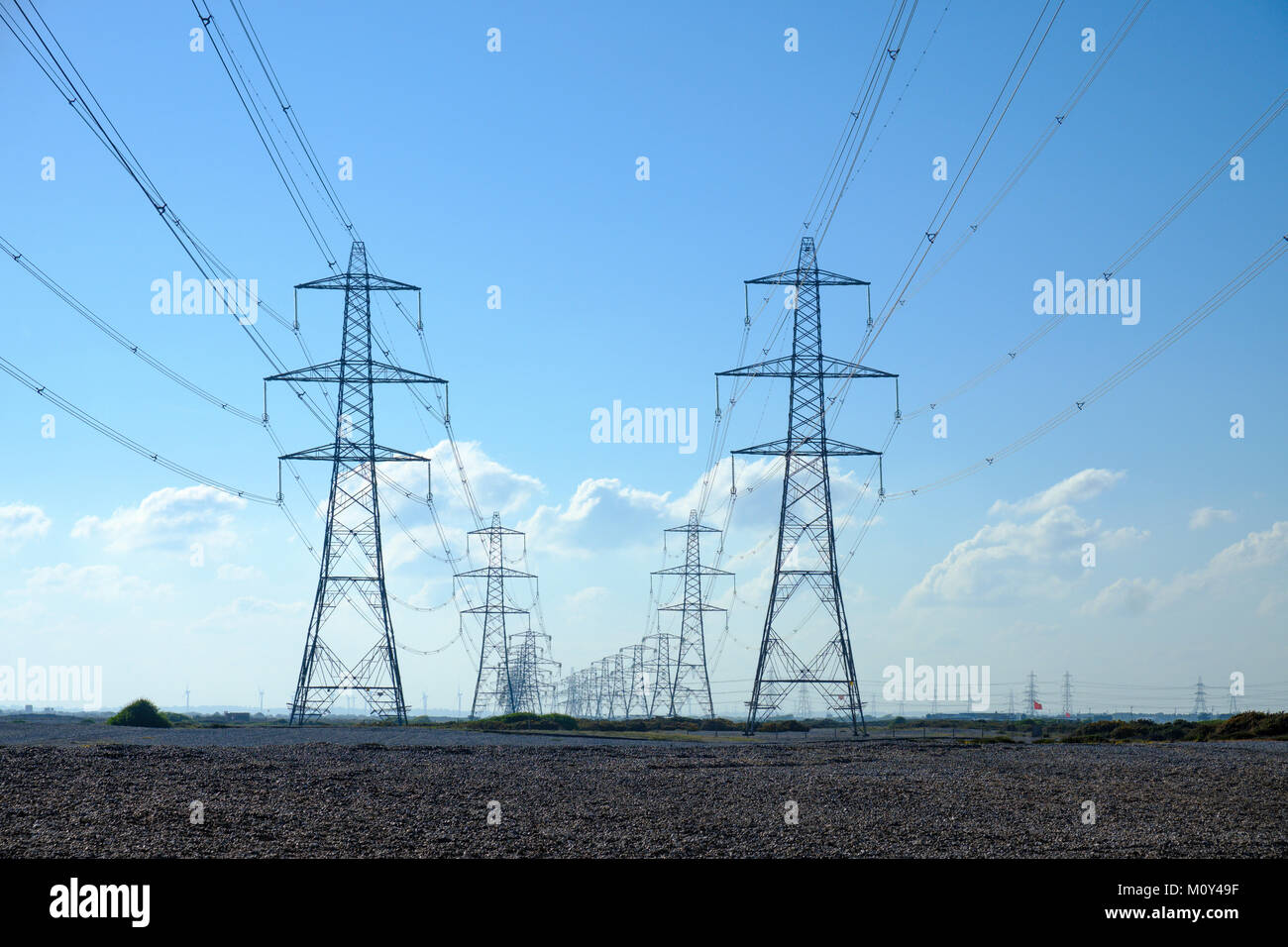 Filas de torres eléctricas (transmisión/torres eléctricas) distribuyen electricidad en el sistema interconectado nacional de energía nuclear de Dungeness, Kent, Inglaterra, Reino Unido. Foto de stock