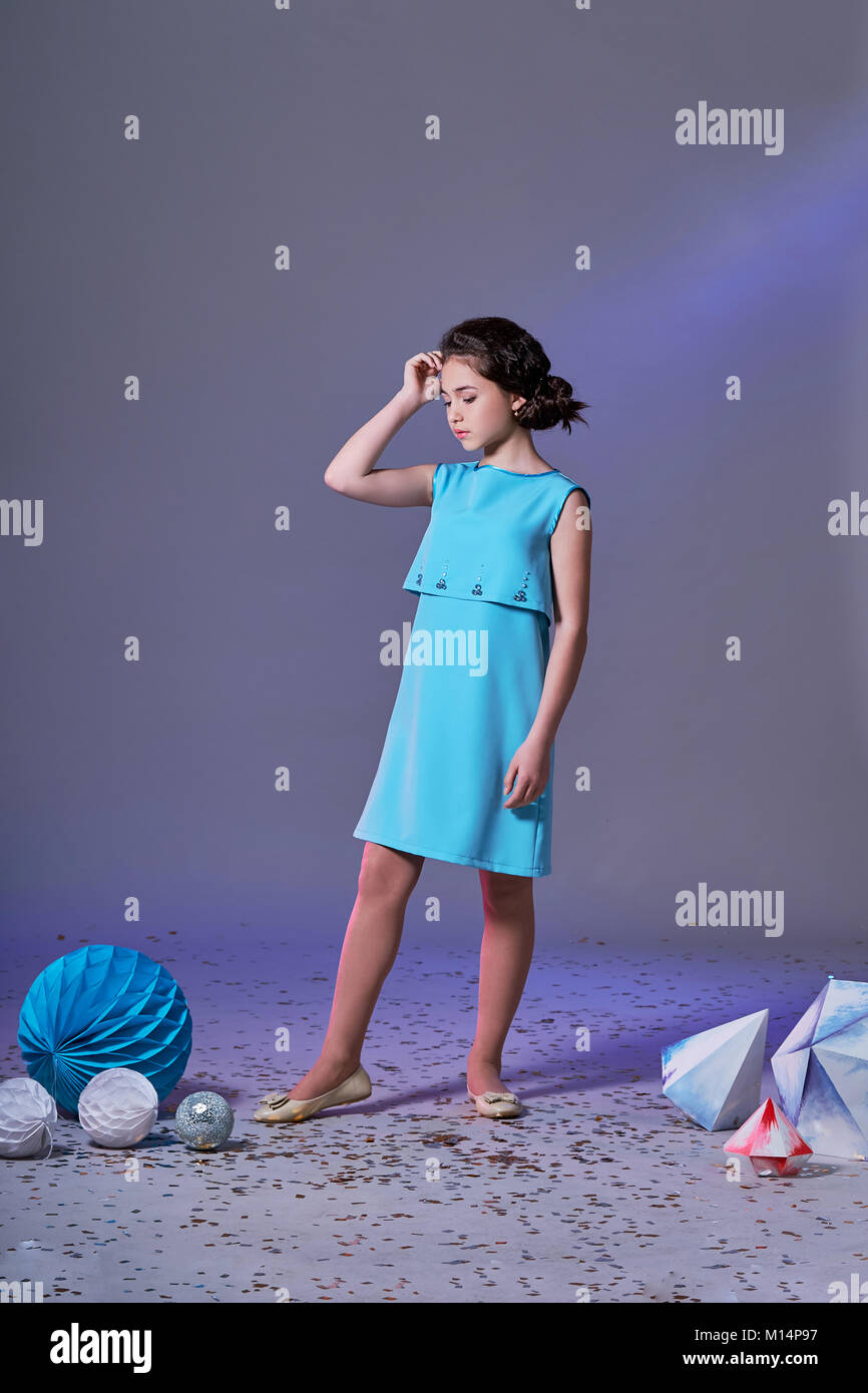 Chica bonita en un elegante vestido azul para niñas adolescentes con un maquillaje. Origami y el minimalismo. Moda niños. Foto de stock