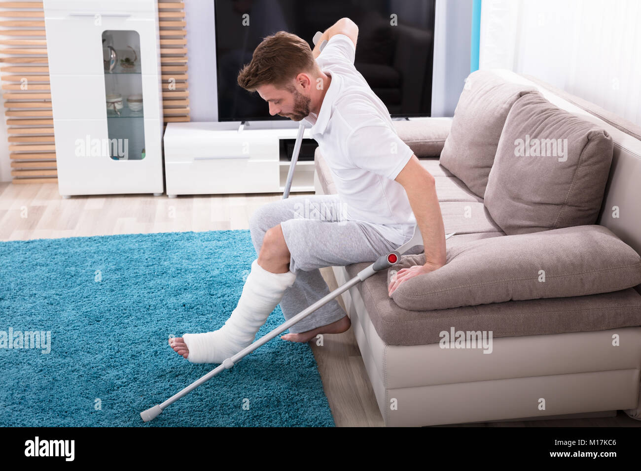 Joven con fractura de pierna con muletas para levantarse del sofá  Fotografía de stock - Alamy