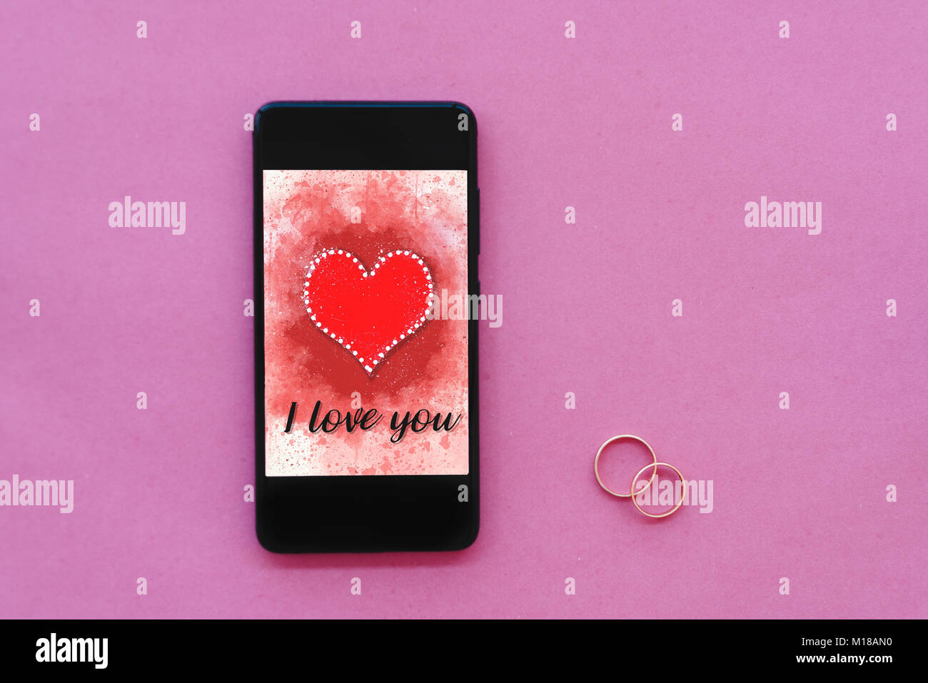 Día de San Valentín venta fondo con corazón ilustración con las palabras I Love You en la pantalla del smartphone boceto sobre fondo de color rosa con dos anillos de boda Foto de stock