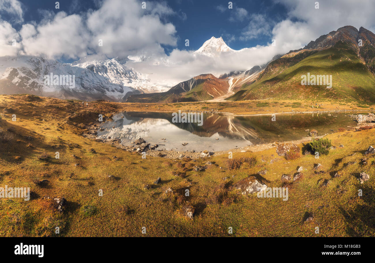 Majestuosas montañas con altas rocas con picos cubiertos de nieve, piedras en Mountain Lake, reflejo en el agua, el cielo azul con nubes en el atardecer. Nepal. Amazi Foto de stock