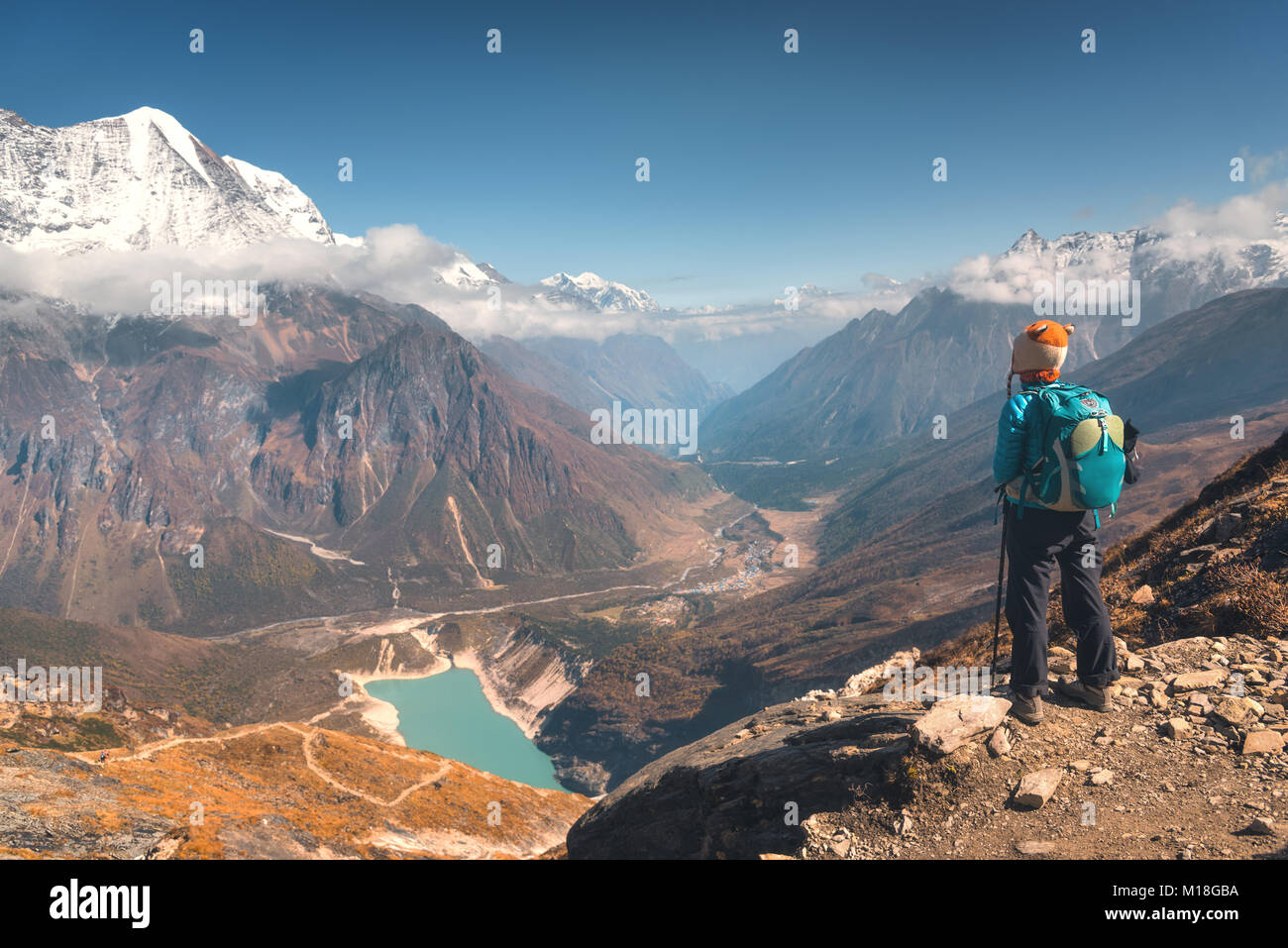 Mujer joven de pie sobre el pico de la montaña y mirar en el hermoso valle de montaña con lago, rocas y colinas al atardecer. Paisaje con muchacha, rocas en Foto de stock