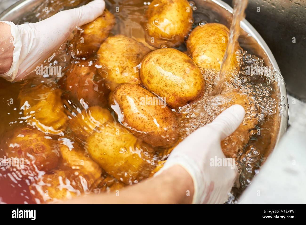 Montones de patatas lavar bajo el grifo de agua. Foto de stock