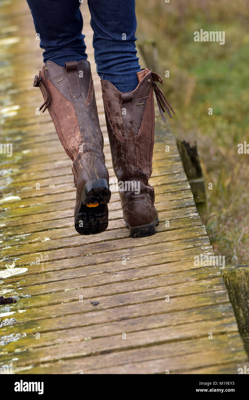 Una mujer caminar en el campo con barro botas de cuero en una vieja  pasarela de madera con jeans y botas de montar en el campo. La moda del  condado Fotografía de