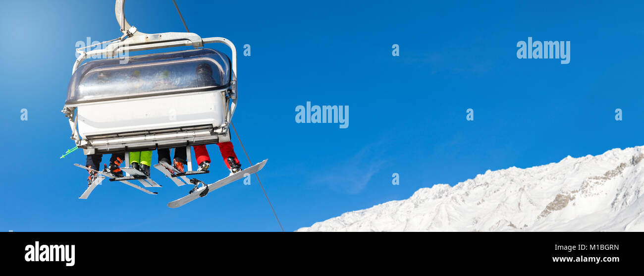 Los esquiadores y snowboarders en un telesquí contra el cielo azul claro. Espacio para texto Foto de stock