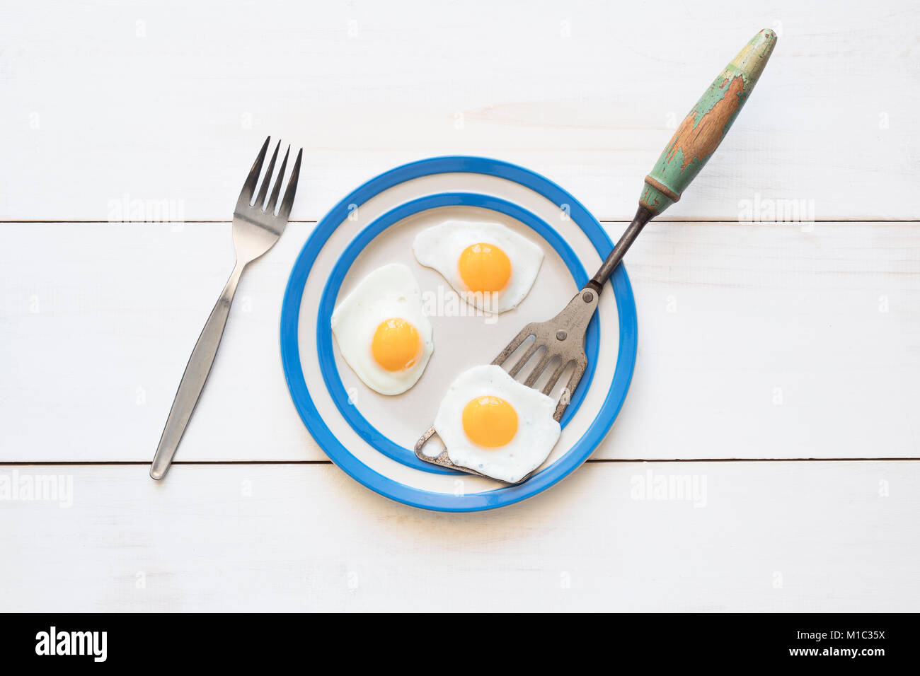 Huevos de codorniz frito sobre una placa cornishware vintage con una espátula y tenedor desde arriba Foto de stock