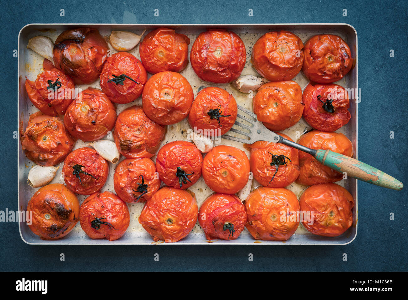 Los tomates asados y el ajo en una bandeja para hornear sobre un fondo