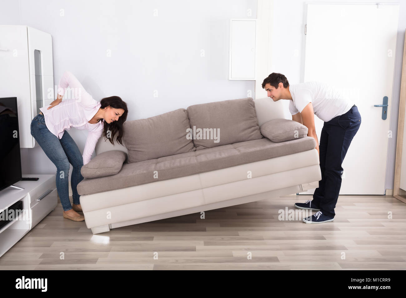 Mujer joven con lumbalgia mientras levanta el sofá con su marido Fotografía  de stock - Alamy