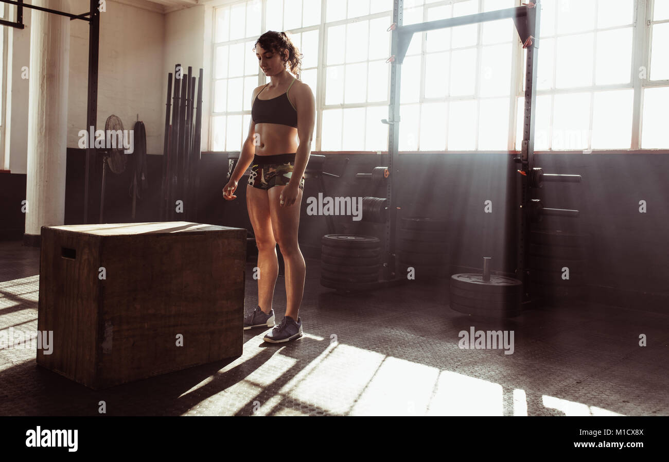 Centrado joven atleta femenina de pie por cuadro saltar al entrenamiento cruzado gimnasio. Musculoso joven que trabaja con un cuadro en el health club. Foto de stock