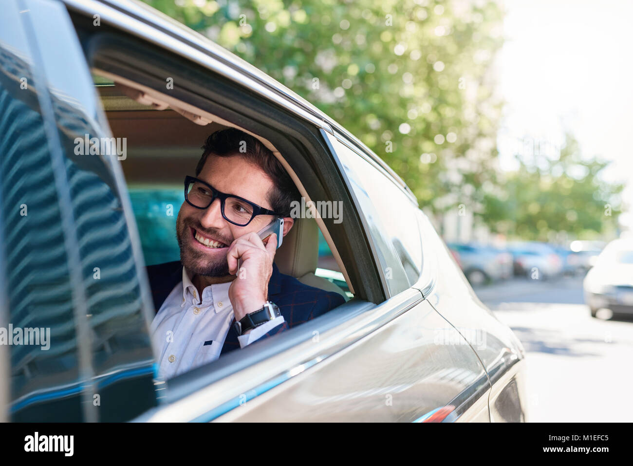 Empresario sonriente conduciendo a través de la ciudad, hablando por un teléfono móvil Foto de stock