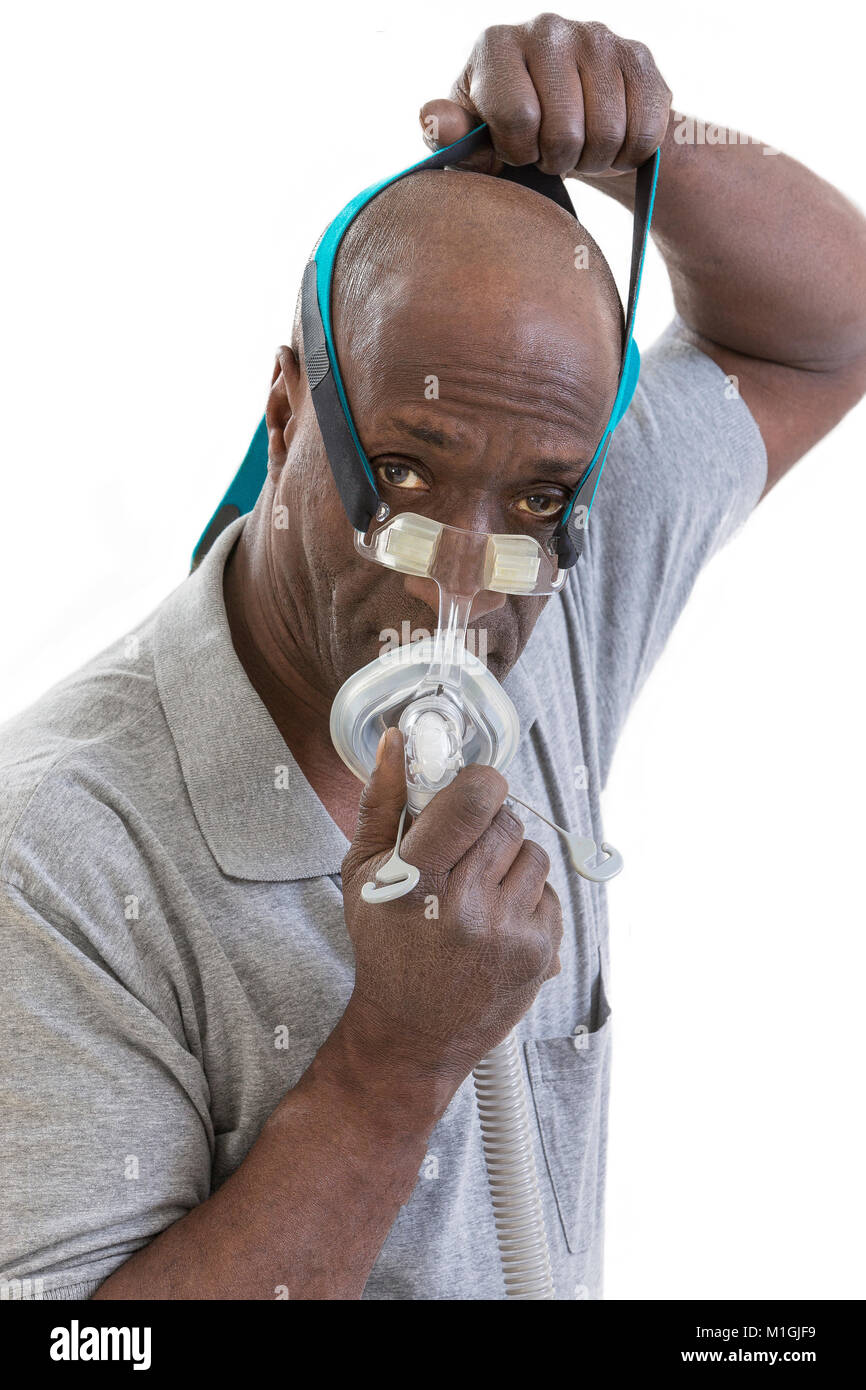 Hombre con un trastorno del sueño trata sobre un Cpap por primera vez, el hombre aprende a ajustar su equipo CPAP sobre fondo blanco. Foto de stock