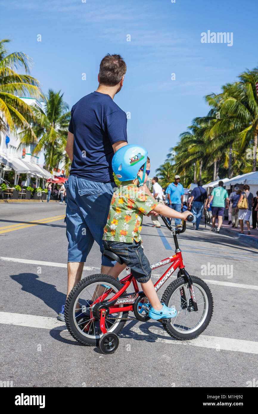 Miami Beach Florida, Ocean Drive, adulto, adultos, hombre hombre varón, niños niños bicicleta, ciclismo, montar, ciclismo, jinete, bicicleta, ruedas de entrenamiento, hel de seguridad Foto de stock