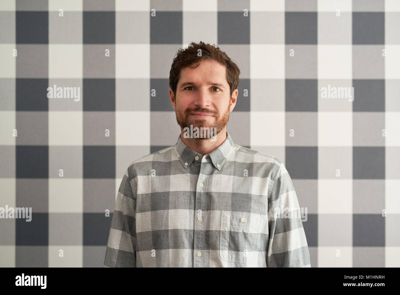 Sonriente joven hombre vestido con una camisa a cuadros igualar su papel tapiz Foto de stock