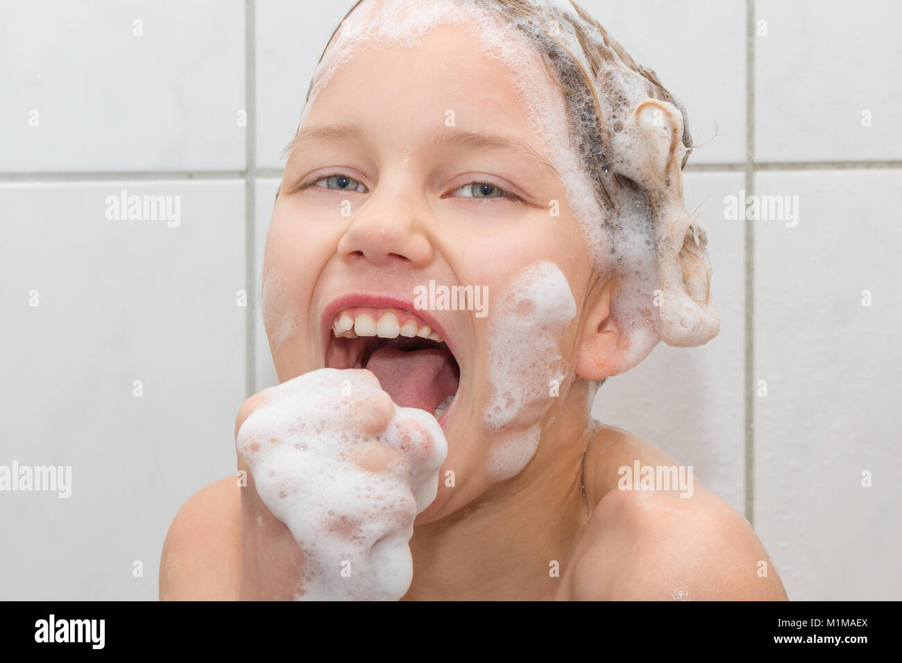 Una niña de 9 años está en la ducha y el canto. Ella constituye un micrófono con su mano Foto de stock