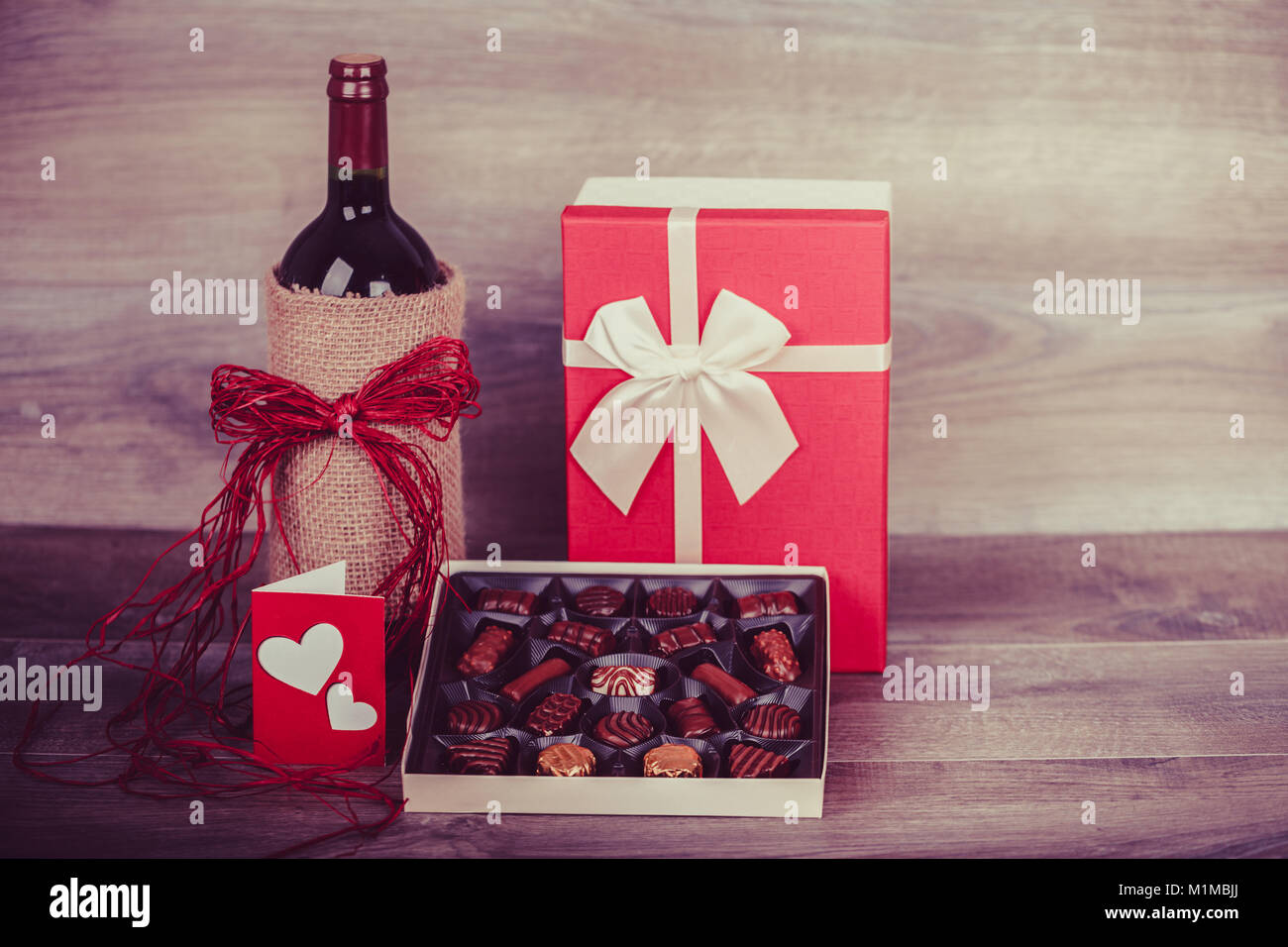 Botella de vino tinto, caja de bombones, mensaje de amor por la decoración  y regalo con corazón rojo sobre la mesa de madera. Concepto de la  celebración del Día de San Valentín.