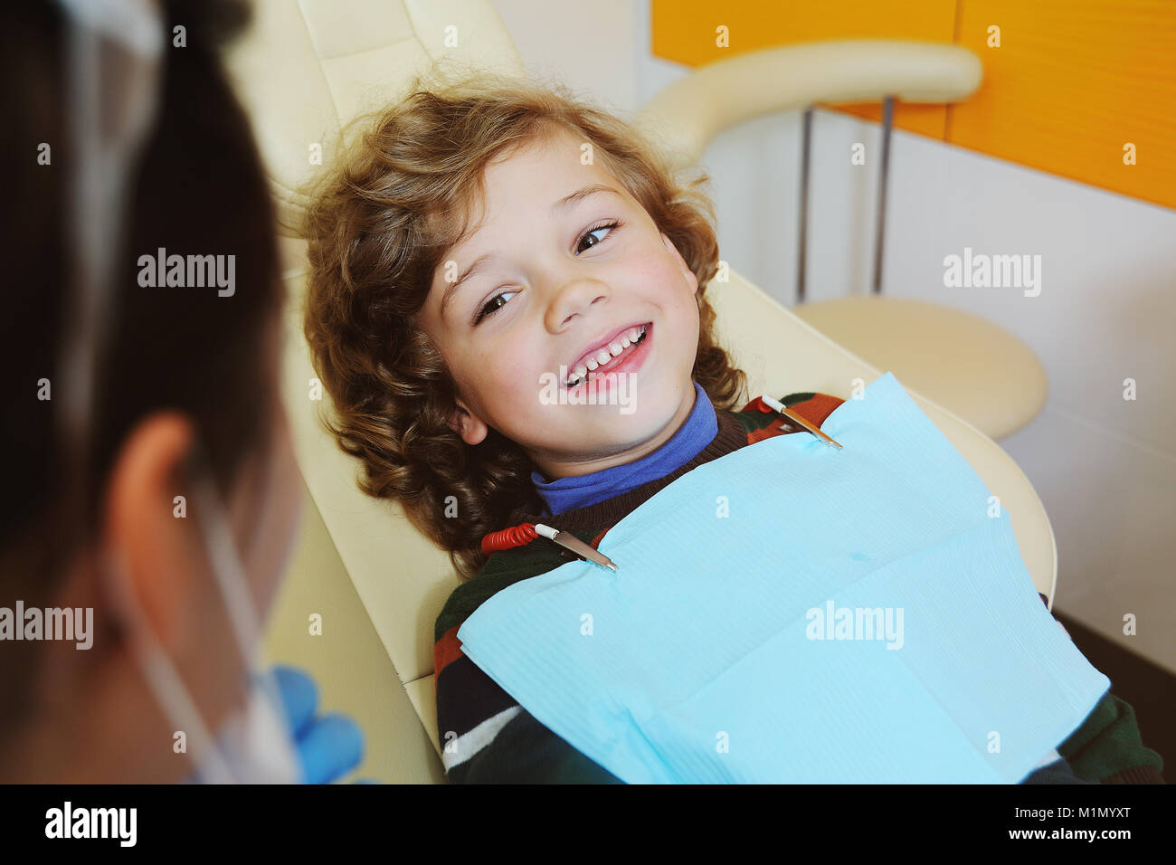 Niño de pelo rizado indulges y muecas en un sillón dental Foto de stock