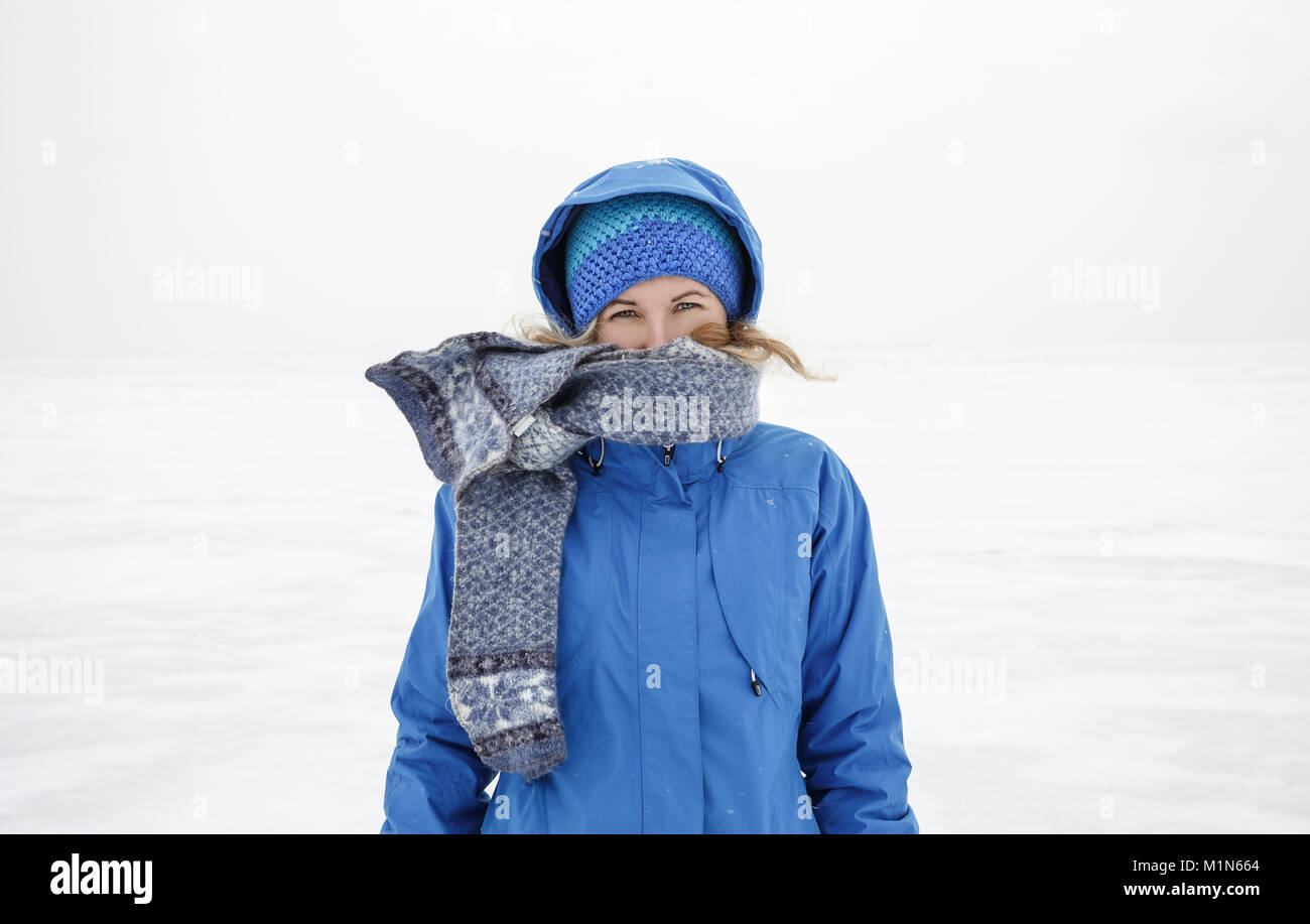 Retrato de mujer con bufanda y chaqueta azul de pie solo en el lago de hielo. Día de invierno nublado frío Foto de stock