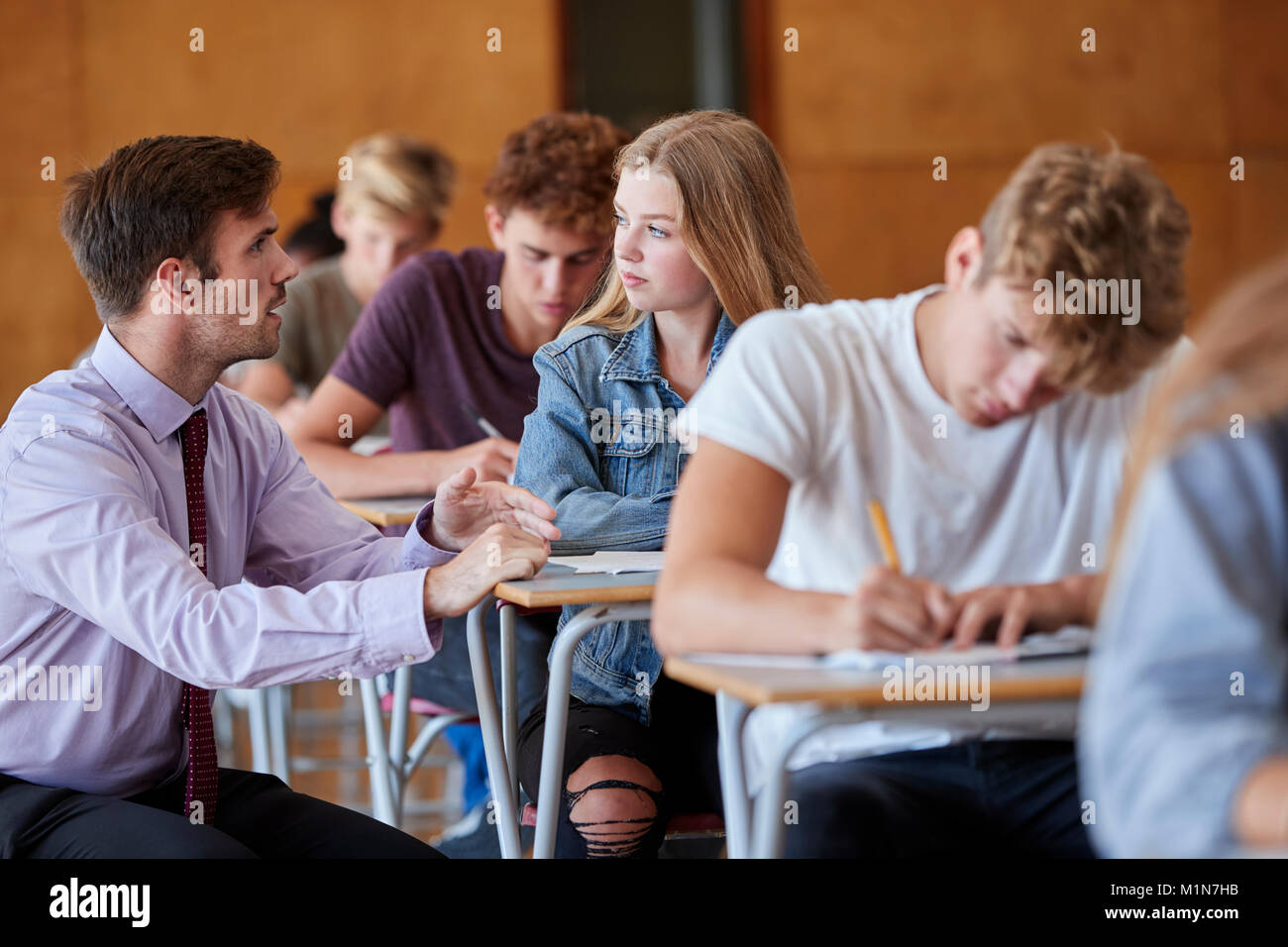 Los estudiantes adolescentes sentados examen con el profesor Invigilating Foto de stock