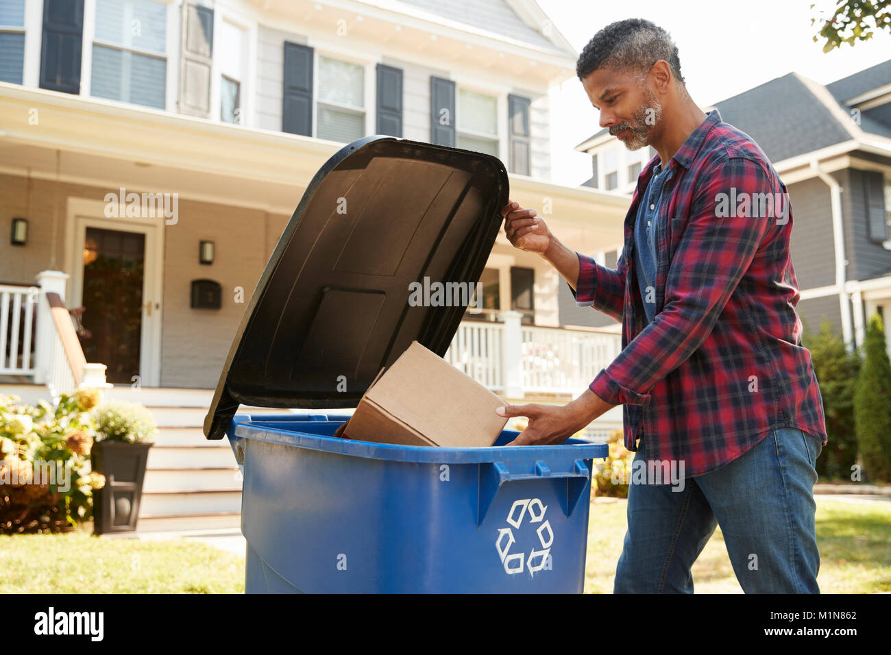 Hombre llenando Papelera de reciclaje en la calle suburbana Foto de stock