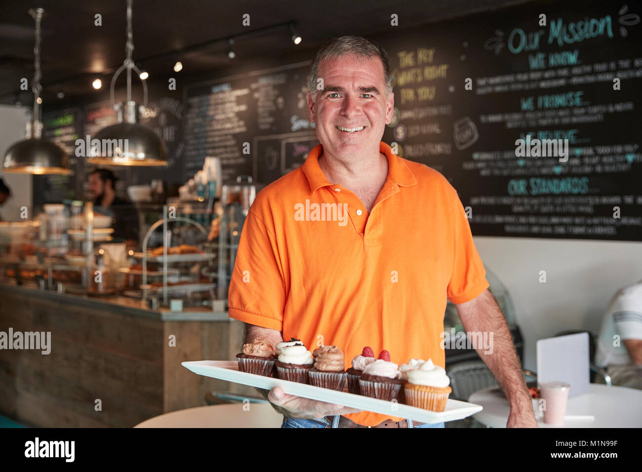 Retrato del propietario masculino con bandeja de muffins en la cafetería. Foto de stock