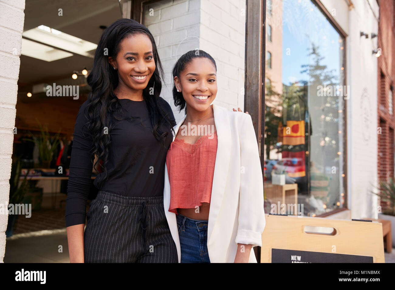 Dos mujeres jóvenes sonriendo a cámara fuera de su tienda de ropa Foto de stock