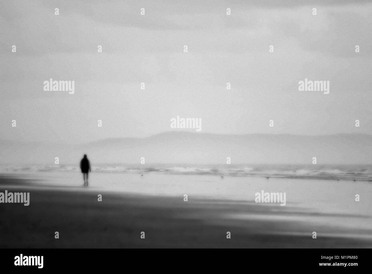 Una foto en blanco y negro de una persona caminando por la playa justo antes del amanecer. Foto de stock